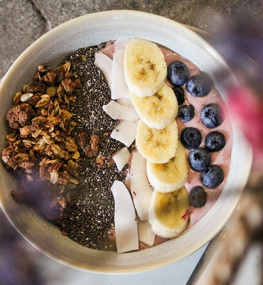 Acai bowl with bananas and blueberries with coconut milk and granola, chia seeds, coconut and almond slices