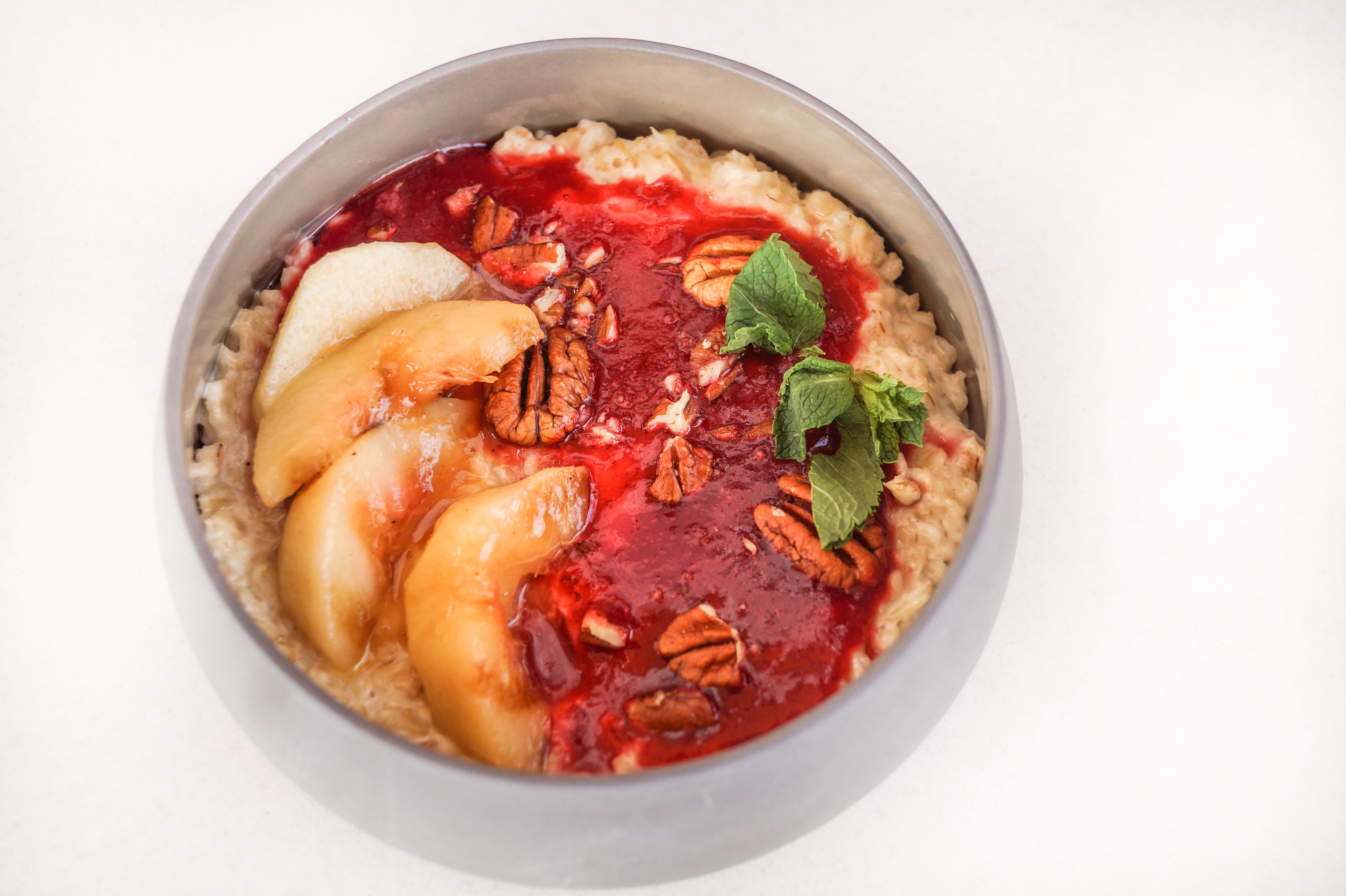 Oatmeal porridge with strawberry sauce, caramelized peaches and pecans