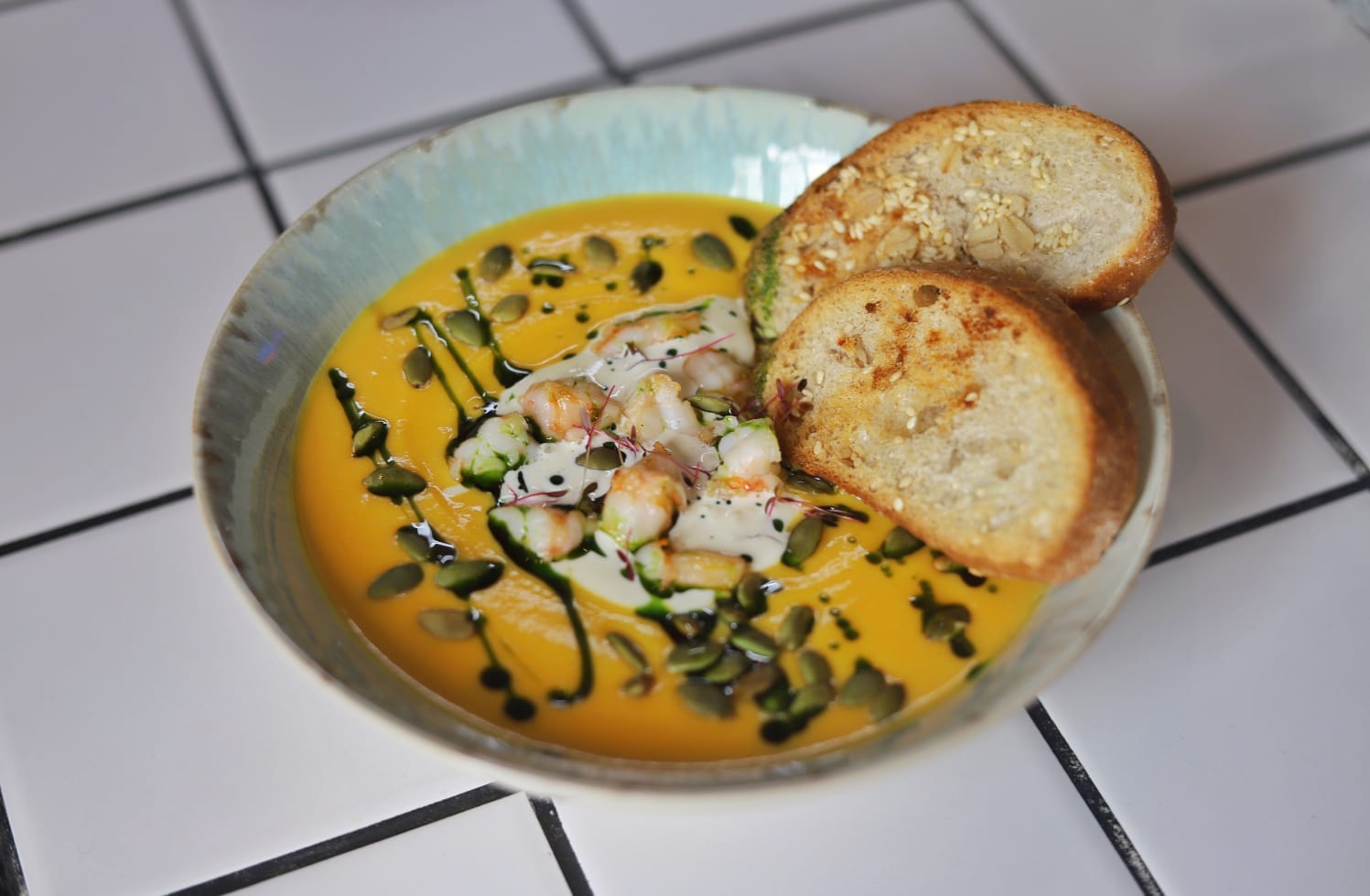 Pumpkin soup with tiger prawns in fragrant herbs, Stracciatella cheese, ciabatta croutons and pumpkin seeds