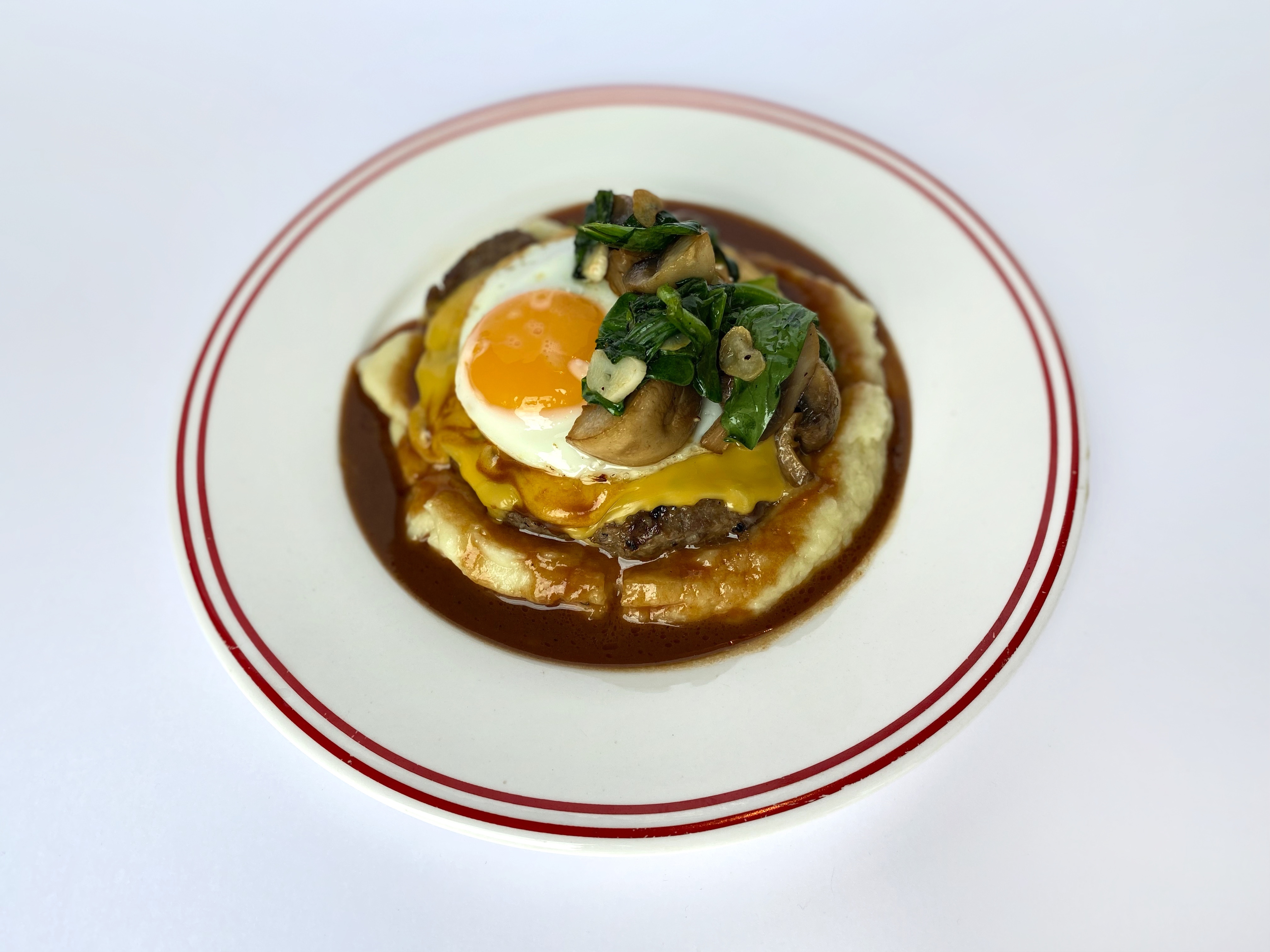 Beefsteak with mashed potatoes, cheddar cheese, fried egg, mushrooms and spinach with stewed meat sauce