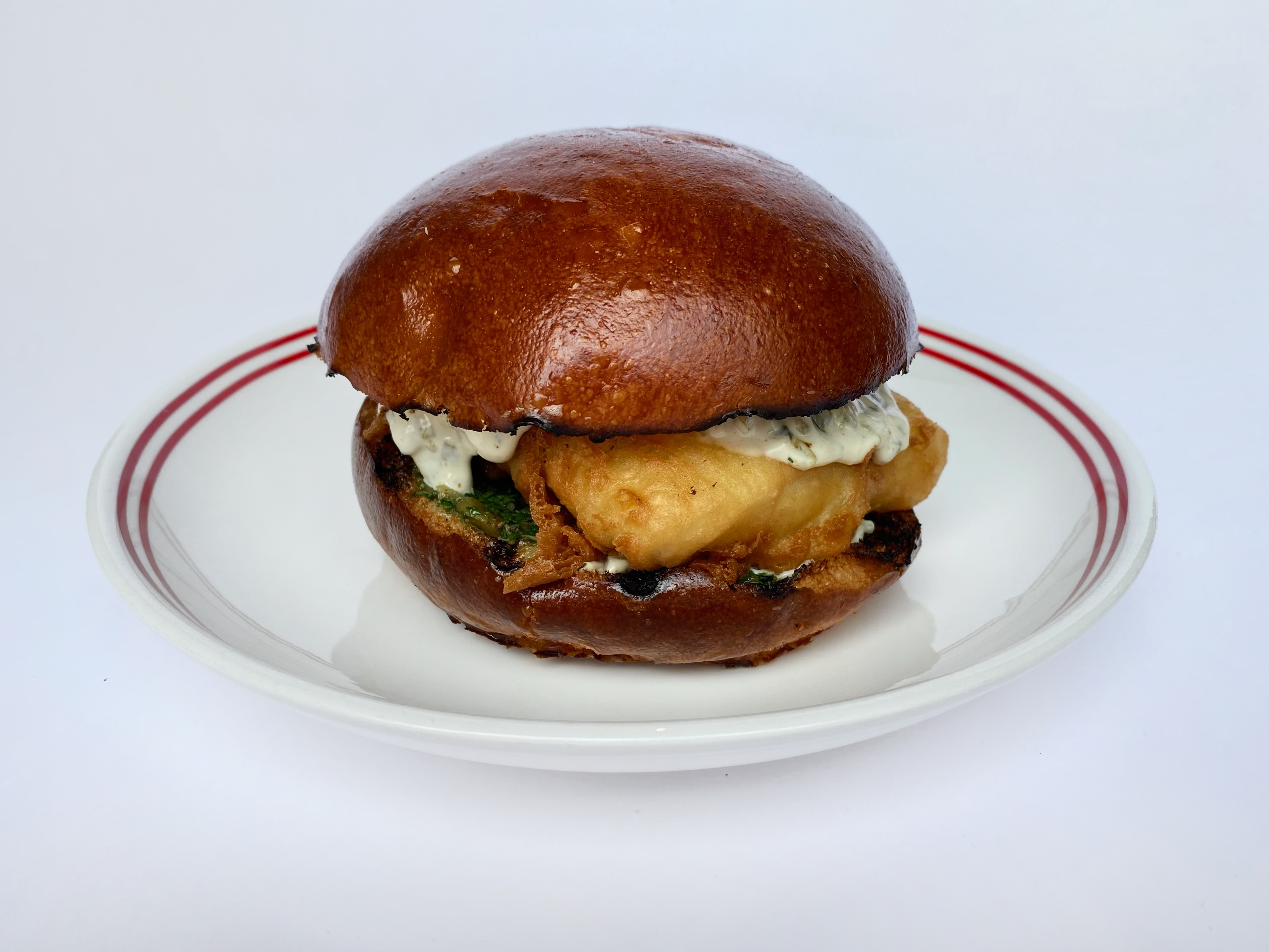 Fish burger with battered cod, brioche bun, red onion and tartar and salsa verde sauces<br>